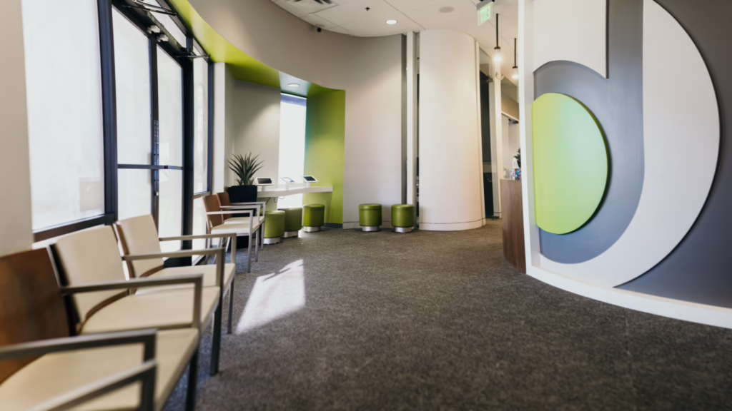 Modern office lobby with beige chairs along a window wall and a large circular blue-green sculpture on the right.